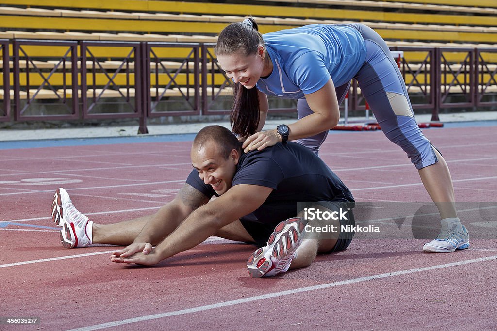 Man and woman at the stadium Two athletes helps each other to stretch at the stadium Active Lifestyle Stock Photo