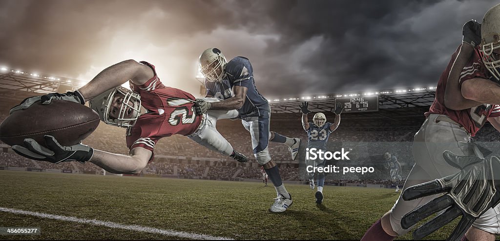 American Football Player in Mid Air Touchdown Tackle Professional american football player diving whilst being tackled during game in outdoors stadium under dramatic sky at sunset. American Football - Sport Stock Photo