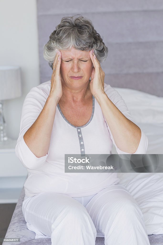Mujer madura sentado en su cama con dolor de cabeza - Foto de stock de 50-59 años libre de derechos