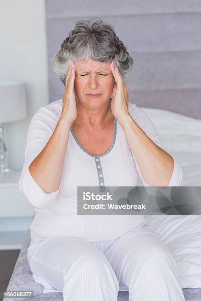 Mujer Madura Sentado En Su Cama Con Dolor De Cabeza Foto de stock y más banco de imágenes de 50-59 años
