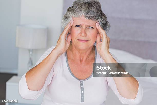 Fruncir El Ceño Mujer Madura Sentada En Su Cama Con Dolor De Cabeza Foto de stock y más banco de imágenes de 50-59 años