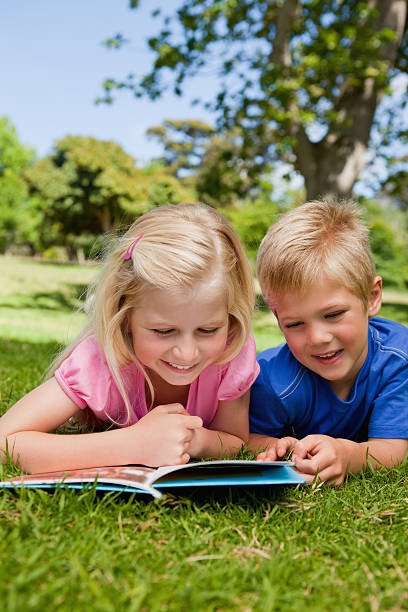 istock Smiling children reading a book in green park 456071429