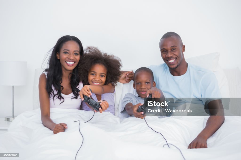 Attraente famiglia seduto nel letto la riproduzione di video giochi - Foto stock royalty-free di Adulto