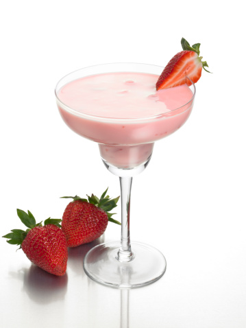 A strawberry daiquiri cocktail, or it could be a smoothie. Shot on a reflective background with fresh strawberries.