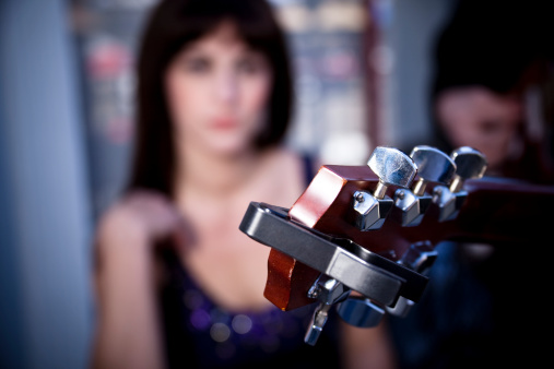 Focus is on the guitar neck, girl in background in soft focus.  