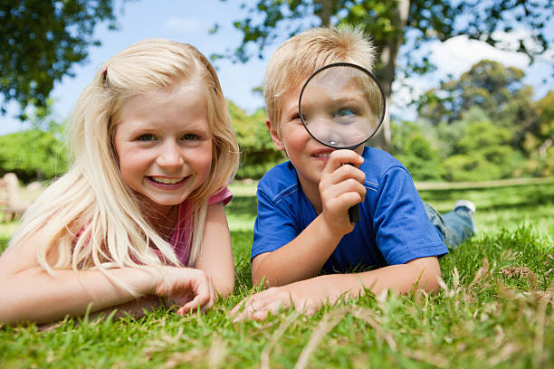 istock Smiling child holding a magnifying glass lying on lawn 456081407