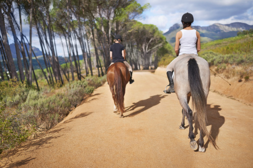 Rear-view of two female riders on horseback trotting down a countryside path