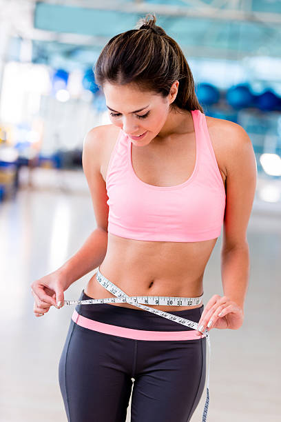 Fit woman measuring her waist Fit woman at the gym measuring her waist exercising tape measure women healthy lifestyle stock pictures, royalty-free photos & images