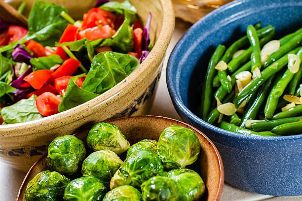 Mixed green salad, cooked brussells sprout and geenbeans in bowls.