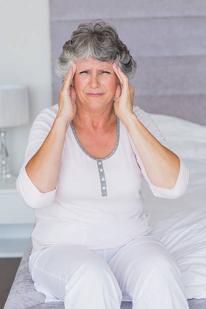 istock Unsmiling mature woman sitting on her bed has headache 456109997