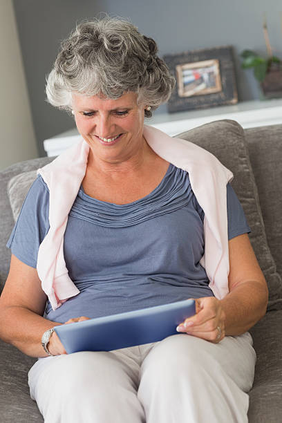 istock Smiling mature woman sitting on sofa using tablet pc 456110017