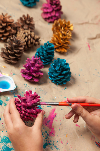 Close-up of child hands painting pine cones for Chrismas decoration. Selective focus on hands.