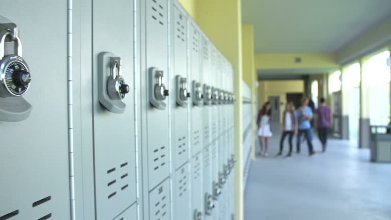 Camera tracks along lockers in high school with students walking along hallway in background.Shot on Sony FS700 at frame rate of 25fps