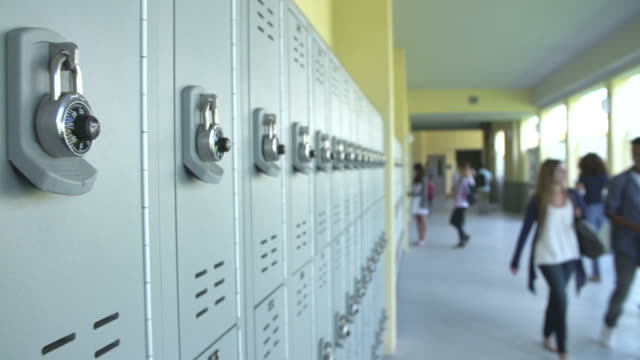Camera tracks along lockers in high school with students walking along hallway in background.Shot on Sony FS700 at frame rate of 25fps