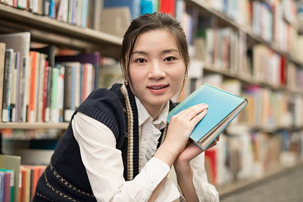 Woman holding a book near bookshelf stock photo