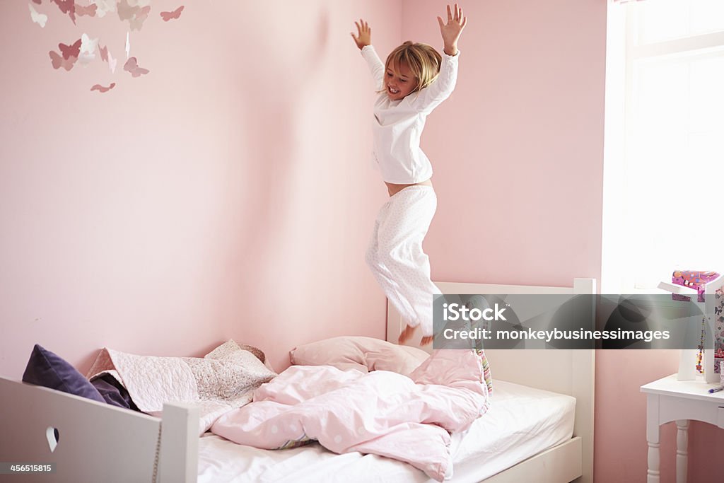 Happy girl jumping on her bed in a pink bedroom Young Girl playing and Jumping On Her Bed Child Stock Photo