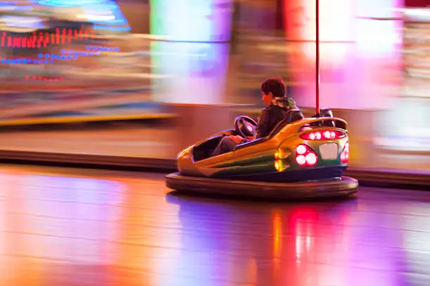 Man driving bumper car in an amusement park at night, blurred motion