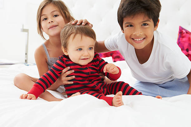 bambino seduto su un letto nel loro pigiama - sibling baby three people baby girls foto e immagini stock