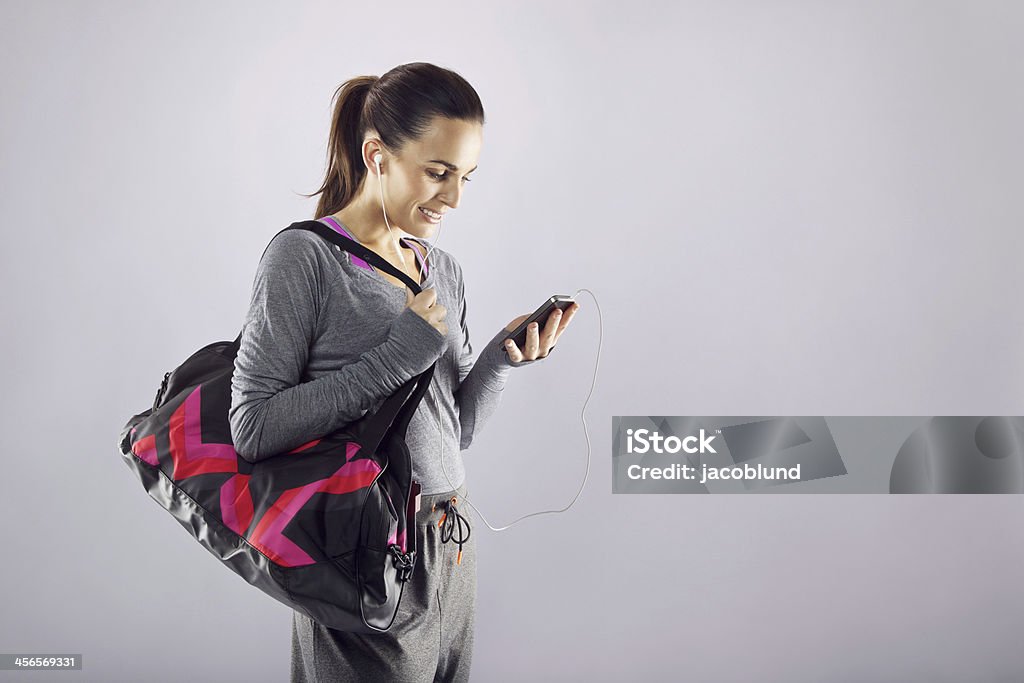 Fitness woman with gym bag listening music Good looking female athlete with a sports bag listening to music on her mobile phone. Fitness woman in sports clothing going to gym on grey background Gym Bag Stock Photo