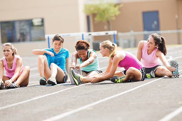 Athletic high school girls stretching on track before race