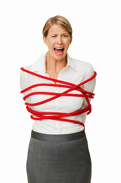 Frustrated Businesswoman Tied In Rope Portrait of frustrated businesswoman tied in red rope screaming against white background. Vertical shot. bound woman stock pictures, royalty-free photos & images