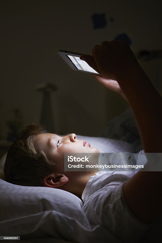 Boy Looking On Digital Tablet In Bed At Night Boy Looking At Digital Tablet In Bed At Night 10-11 Years Stock Photo