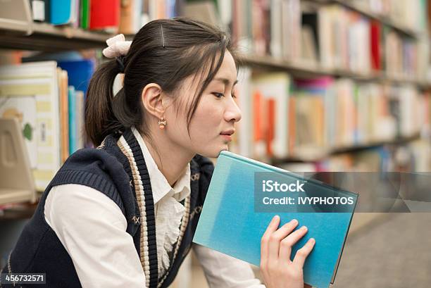 Foto de Mulher Segurando Um Livro Perto Estante e mais fotos de stock de Adulto - Adulto, Aluno de Universidade, Aprender