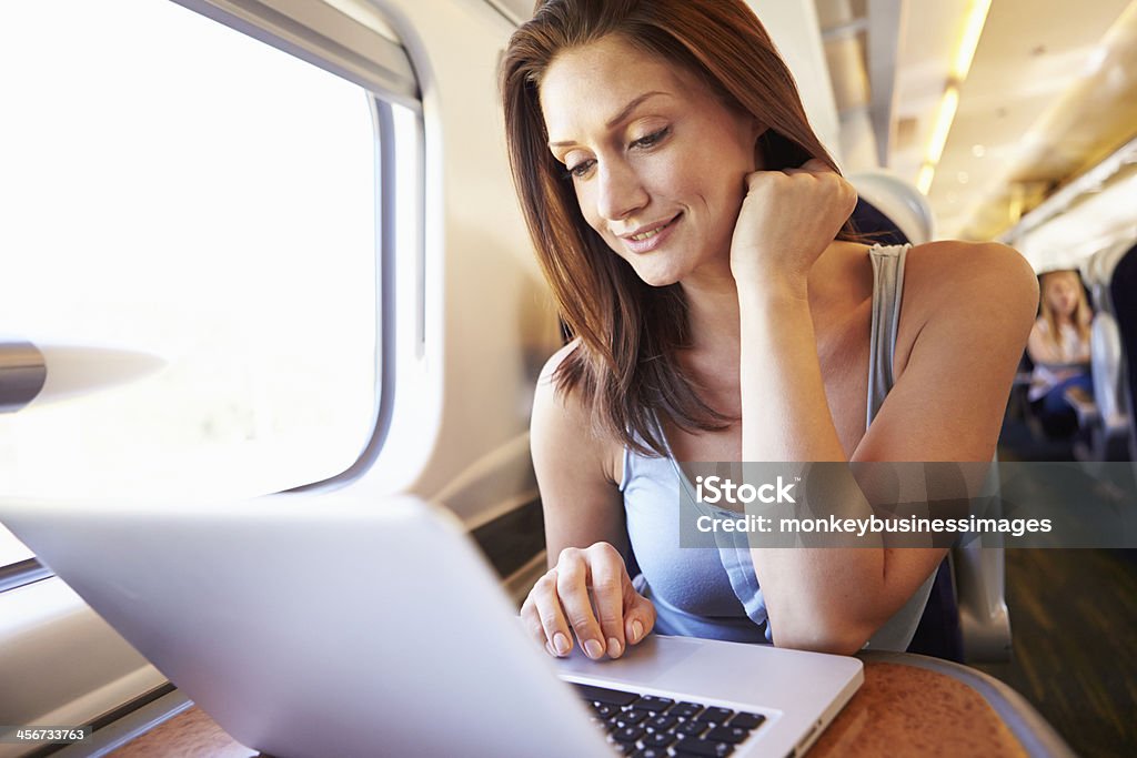 Woman enjoying her commute on a train with a laptop at hand  Woman focussing on Laptop On Train 30-39 Years Stock Photo