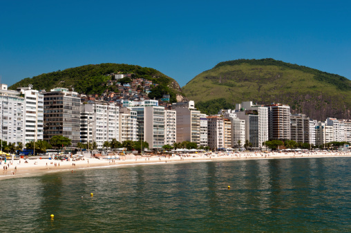 Luxury residential apartment and hotel buildings in the front of the Copacabana beach with mountains behind in Rio de Janeiro, Brazil.