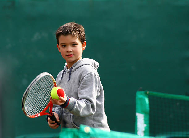 piccolo giocatore di tennis su un offuscata backround verde - tennis child teenager childhood foto e immagini stock