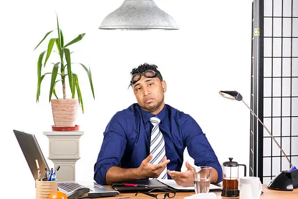 An image of an Indian office worker with a blue shirt behind his desk