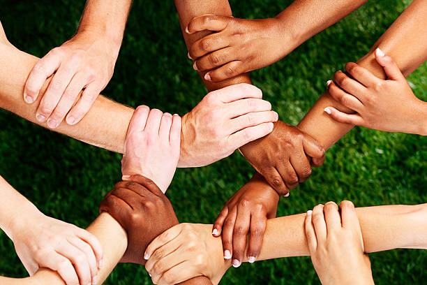 Complex linking of many mixed hands: unity is strength! Many multiracial male and female hands are joined together in unity, forming a complex linked shape, against grass. Together we are stronger!  black civil rights stock pictures, royalty-free photos & images