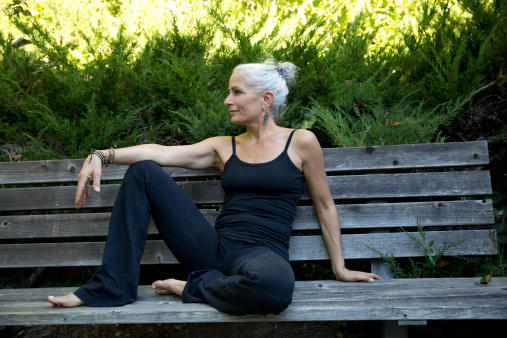 grey-haired woman sitting on a bench in the shade, after doing yoga