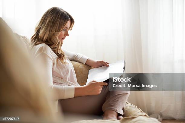 Woman Sitting On Sofa Reading Magazine Stock Photo - Download Image Now - Reading, Magazine - Publication, One Woman Only