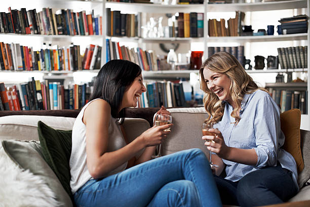 women sitting on sofa laughing - drinking wine stockfoto's en -beelden