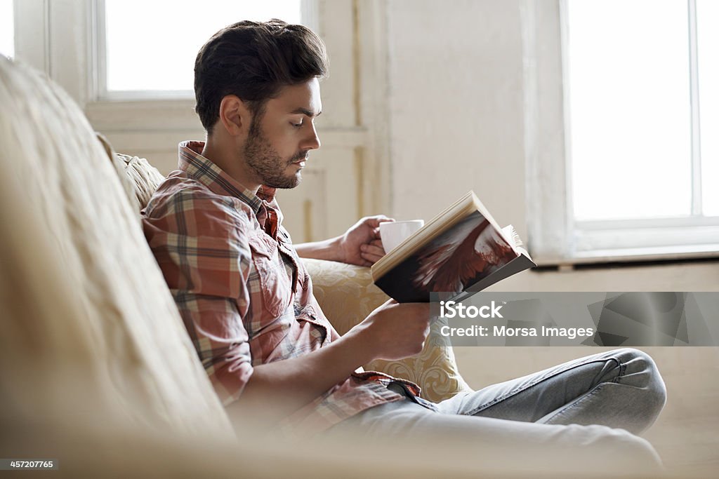 Man sitting on sofa reading book Man sitting on sofa reading a book in a cozy loft apartment Reading Stock Photo