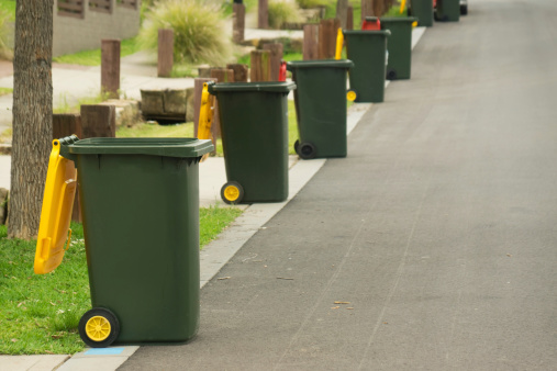 Row of wheelie bins emptied on bin day in suburban western Sydney. Yellow for recyclable material, red for general waste.