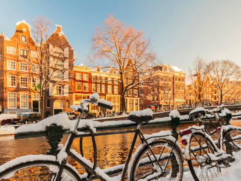Bicycle leaning against the canal railings in Amsterdam, sunny and cold winter day. Beautiful cityscape of Amsterdam. Typical Dutch canal surrounded by trees. Sun shining and creating long shadows.  Travel destination and transport background, copy space.