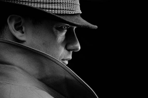 Mysterious detective A black and white portrait of a mysterious detective wearing a trilby hat against a dark background. film noir style stock pictures, royalty-free photos & images