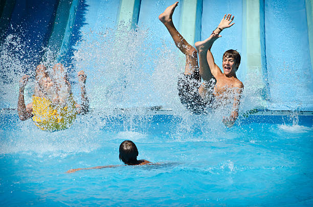 Headshot of a teenage boy, 13 years old, having fun at a water park, a giant water slide out of focus behind him. He is grinning at the camera.