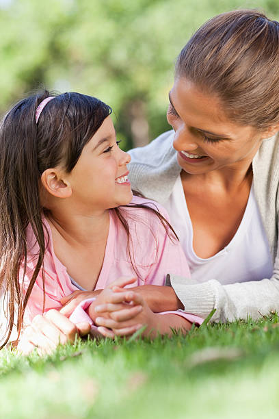 istock Mother and daughter lying on lawn smiling at each other 457425489