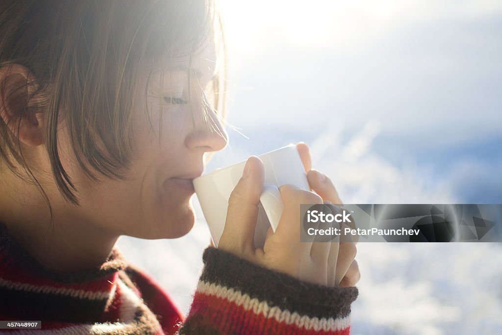 Woman drinking a hot drink while wearing a sweater Beautiful young woman drinking hot drink outside on a sunny cold winter morning Adult Stock Photo