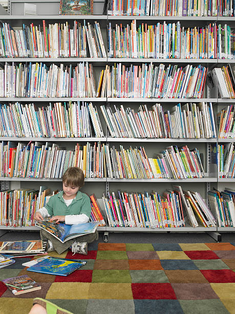 istock Young boy sitting on floor reading book at a library 457449037