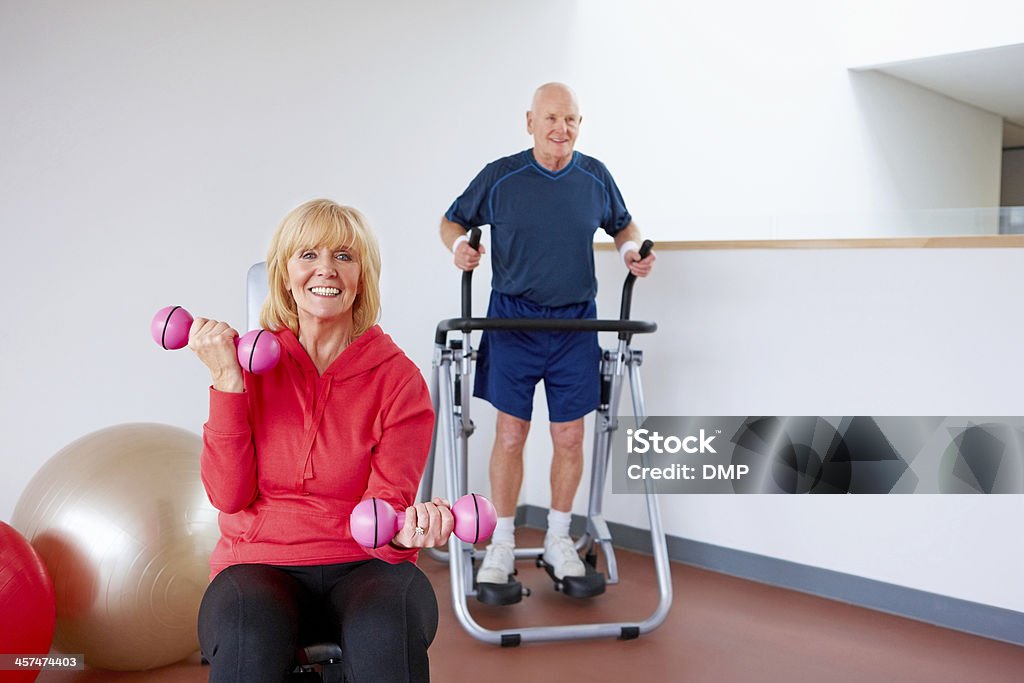 Senior people exercising in the gym Healthy senior woman exercising with dumbbells while a man uses an elliptical machine in the gym 60-69 Years Stock Photo