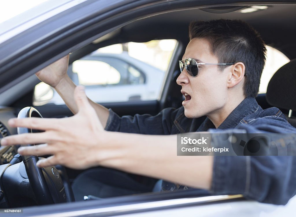 A driver in sunglasses pulling an irritated gesture Irritated young man driving a car.  Road Rage Stock Photo