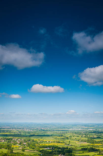 Deep blue skies and white fluffy clouds drifting over a vibrant geen summer landscape of patchwork fields, farms, country homes and rural towns. ProPhoto RGB profile for maximum color fidelity and gamut.