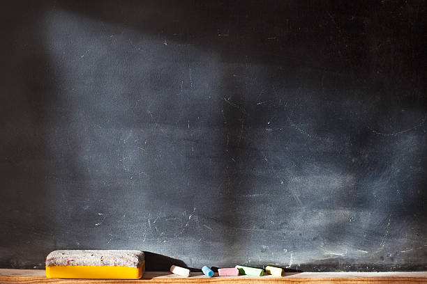 Blank blackboard with colored chalks and eraser and light effect. Horizontal composition.