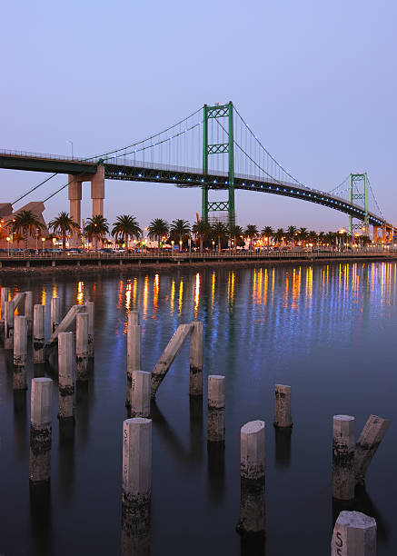 Los Angeles Harbor and The Vincent Thomas Bridge A view of the Port of Los Angeles in San Pedro, California, USA. This photo was taken at dusk. Decorative blue light bulbs on the bridge are lit.  The foregound is dominated by cement pylons emerging from the water. Bright reflections of lights and the bridge towers are seen.  san pedro los angeles photos stock pictures, royalty-free photos & images