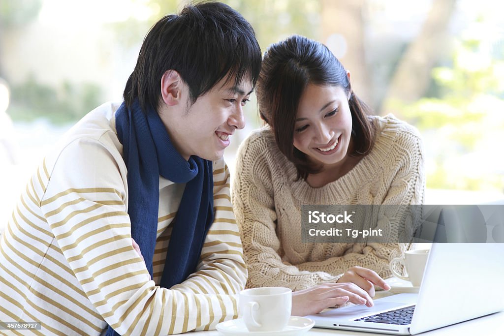 Man and woman sat smiling at laptop with cup and saucer A young couple is searching some information on the Internet. Smiling Stock Photo