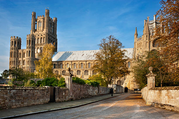 Magnificent Cathedral at Ely towers above small streets in sunshine Ely Cathedral, cathedral, Minster, church, place, places of worship, ancient, trees, clouds, silhouette, stone, autumn, fall, warm, bright, reflection, lead, isolation, city, English, England, Ely, Cambridgeshire, religion, holy, sacred, river, historic, tower, steeple, flint, nature, tranquil, landscape, rural, street, pavement, stained glass, Bench, seat, gravel, path, entrance, doors, porch ely england photos stock pictures, royalty-free photos & images
